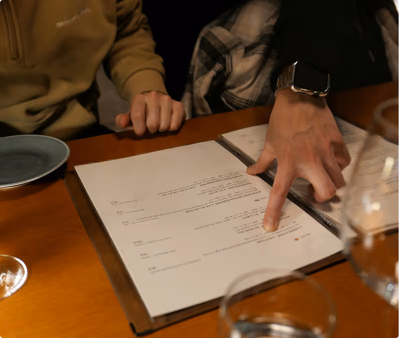 Two people sitting at a table with one pointing to an item on a restaurant menu.