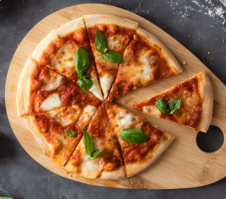 Cheese pizza with tomato sauce and basil leaves on a wooden cutting board with one slice pulled out.