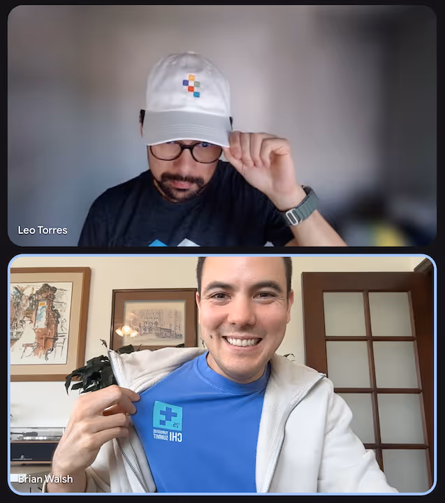 Two men in a video call; the top man wearing glasses and a white cap with a colorful logo, the bottom man smiling, showing a blue t-shirt with a logo reading 'CHI Summit'.