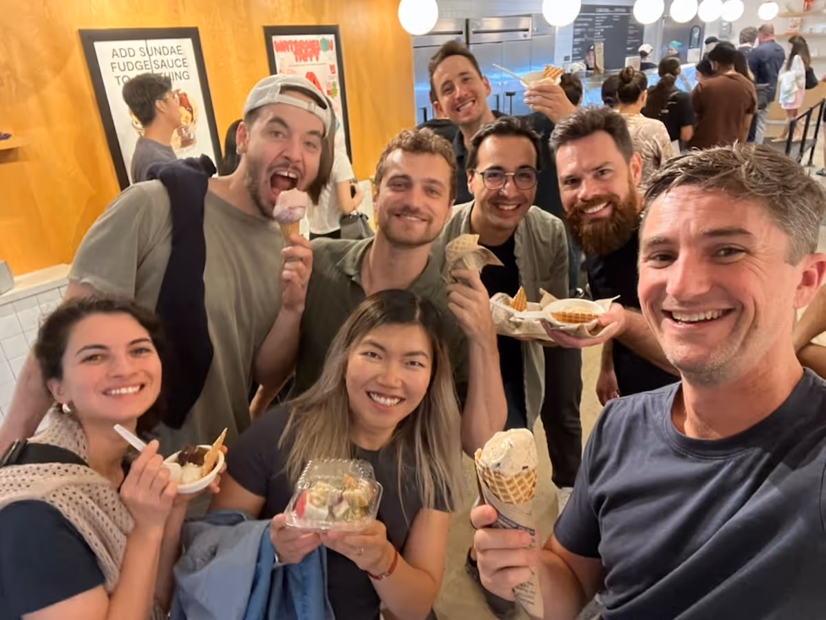 Group of seven smiling people holding ice cream cones and bowls inside an ice cream shop.