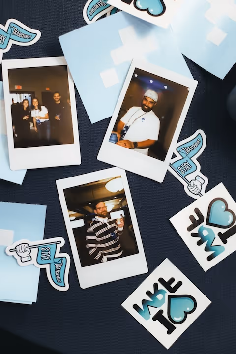 Three Polaroid photos of people on a dark surface surrounded by blue and white stickers with phrases like 'Stay Transparent' and 'We Love To'.