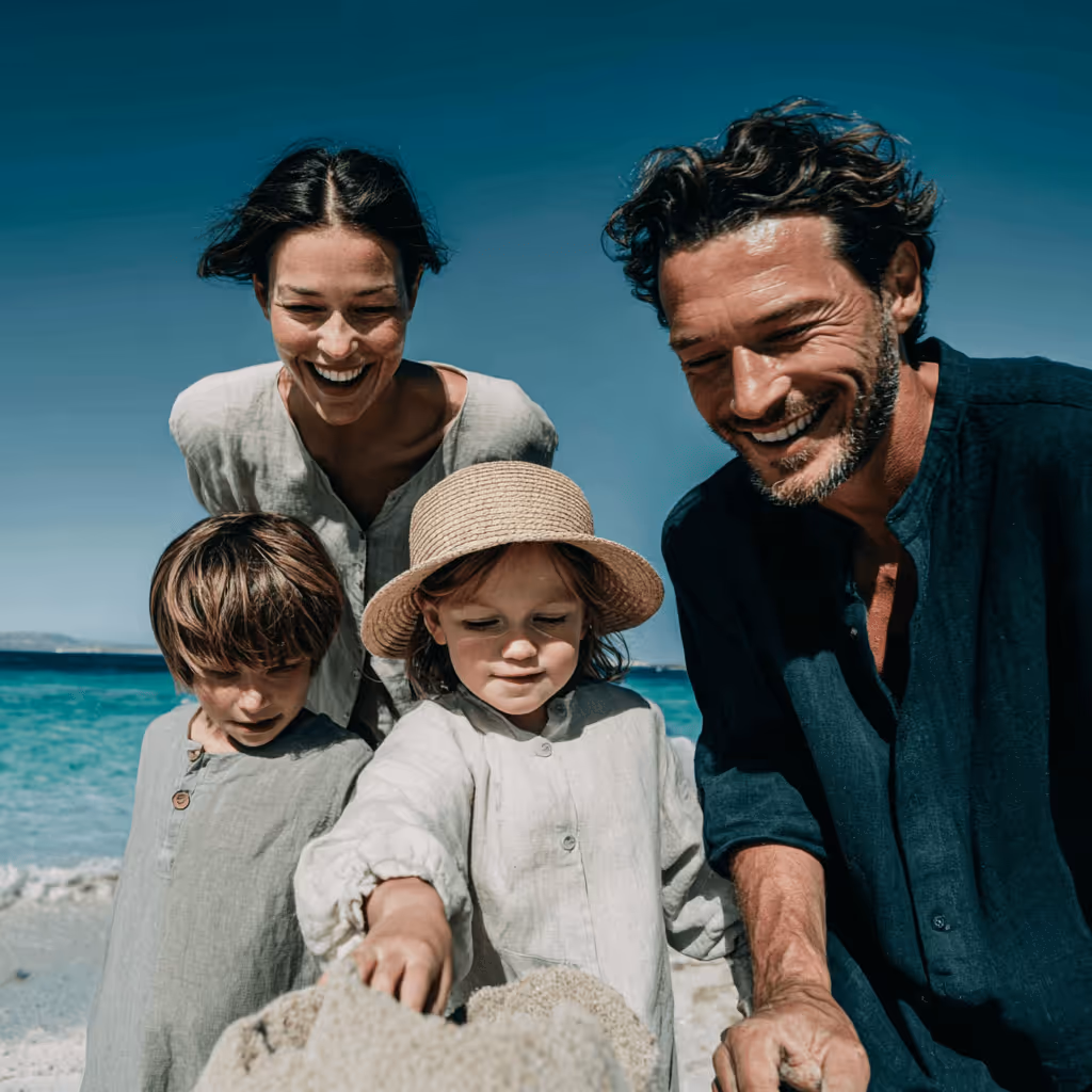 Famille de quatre personnes souriante jouant sur une plage en bord de mer sous un ciel bleu clair.