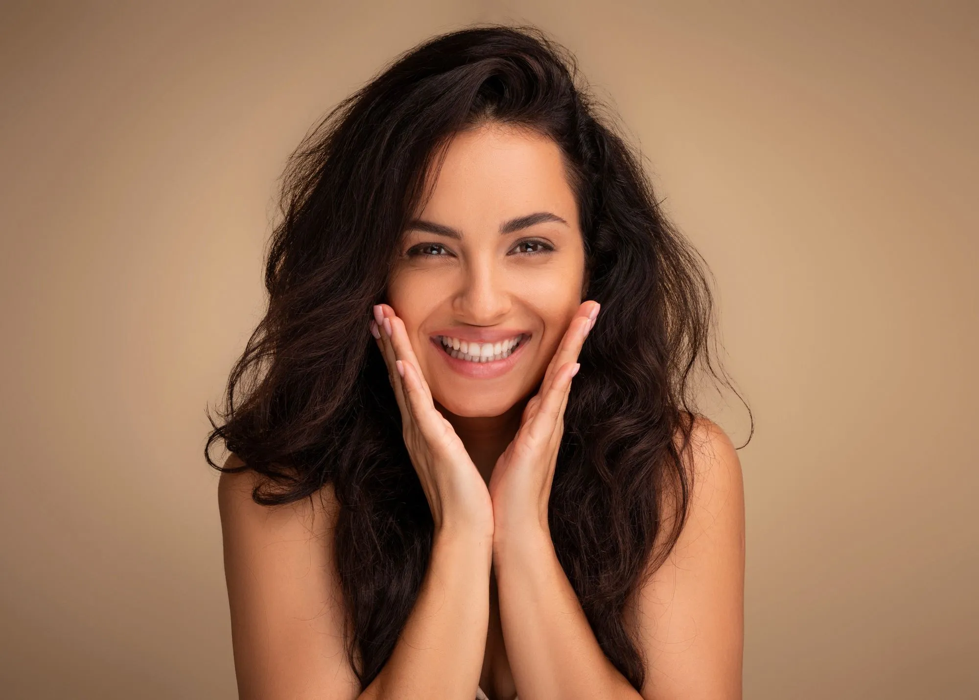 A woman smiling, touching her face