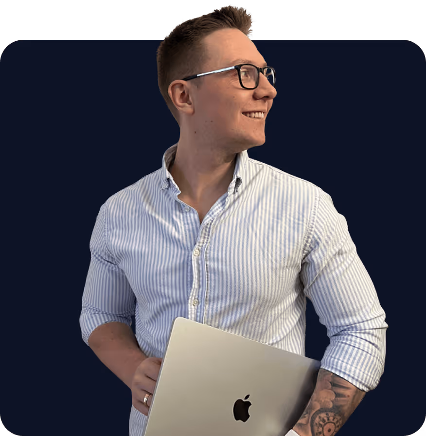 Uśmiechnięty mężczyzna w okularach i pasiastej koszuli trzymający srebrnego laptopa Apple.