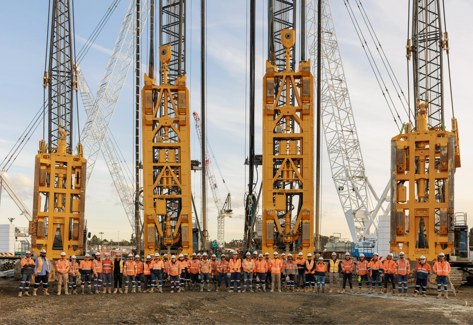 Wide grayscale shot of a large construction crew posing in front of multiple heavy drilling rigs.