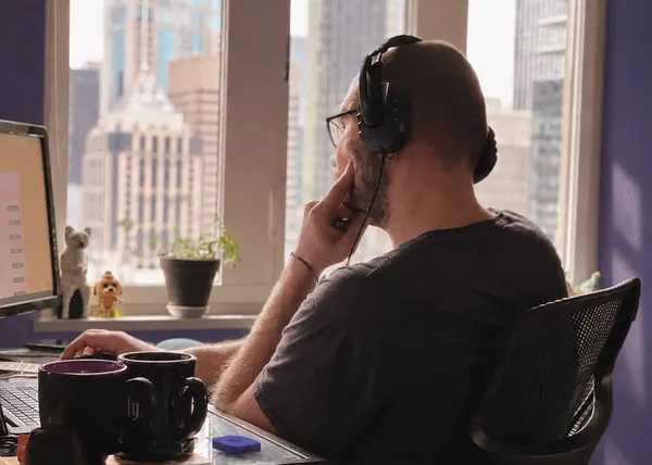 Person wearing headphones working at a computer by a window overlooking city buildings