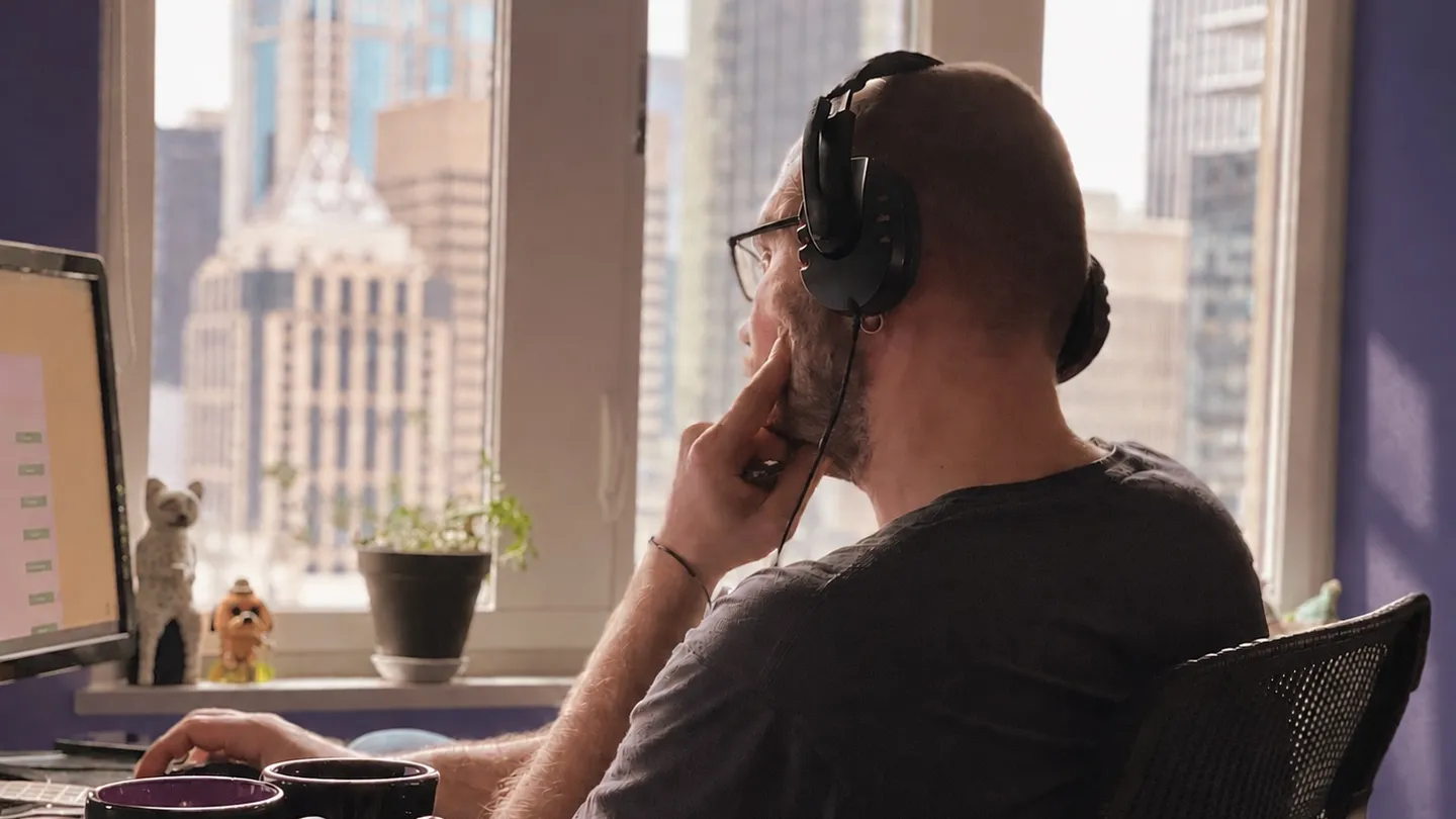 Person wearing headphones working at a computer by a window overlooking city buildings