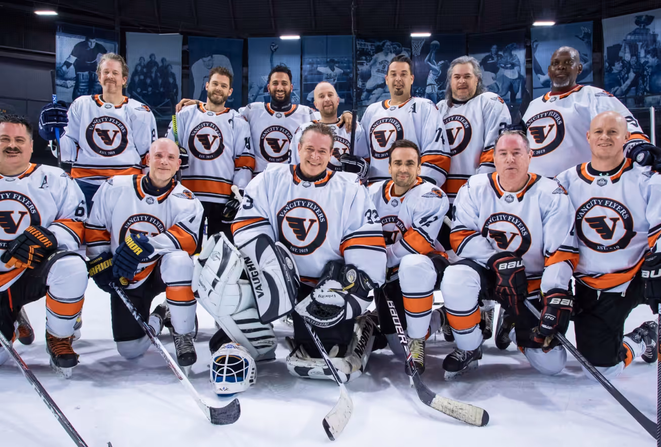 Men's adult ice hockey team Vancity Flyers posing together on ice rink in white jerseys.