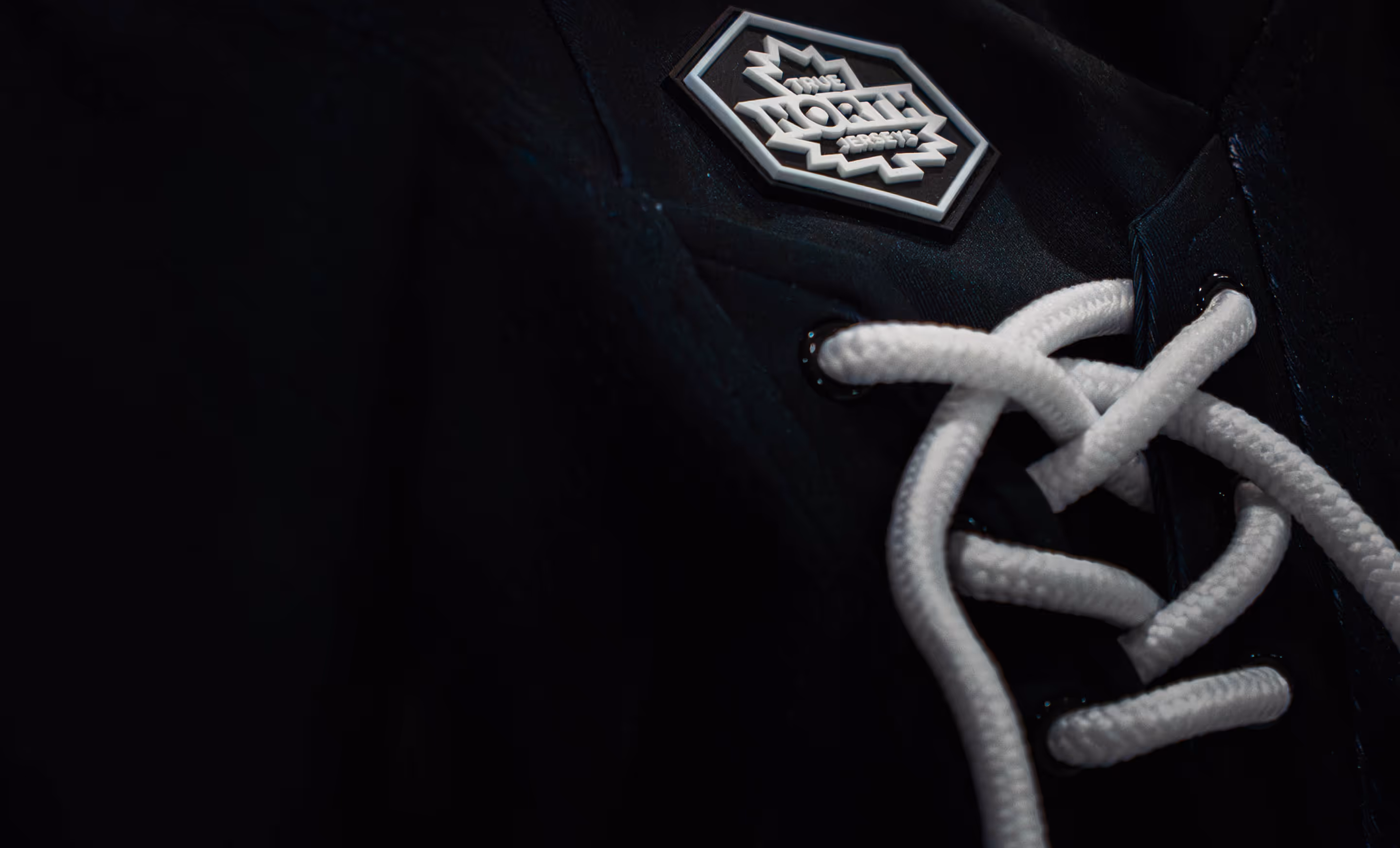 Close-up of black fabric with white lace-up cords and a hexagonal patch reading 'True North Jerseys'.