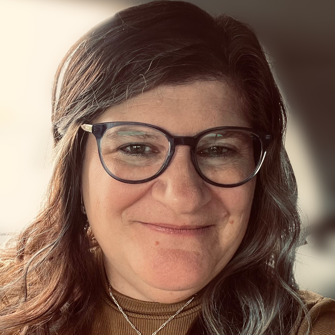 Headshot of Michele McCrary smiling, wearing glasses and a brown top.