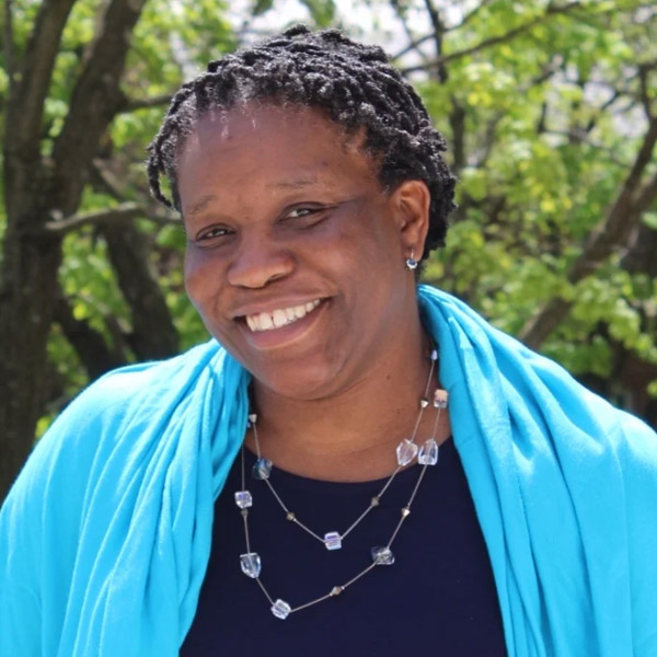 Headshot of Michelle Whittaker smiling outdoors, wearing a blue scarf and necklace.