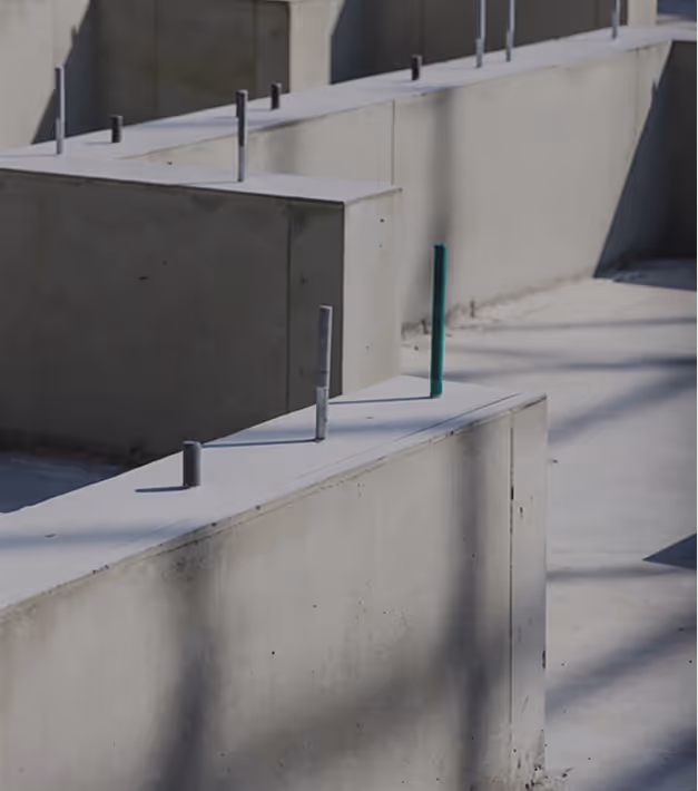 Close-up of concrete walls with metal rods protruding, casting shadows on the surface.