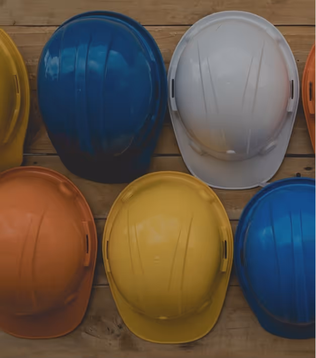 Six construction safety helmets in blue, white, yellow, and orange arranged on a wooden surface.