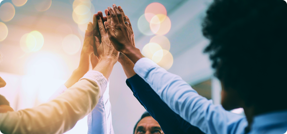 A diverse group of people giving a high-five together in a bright room with bokeh lights.