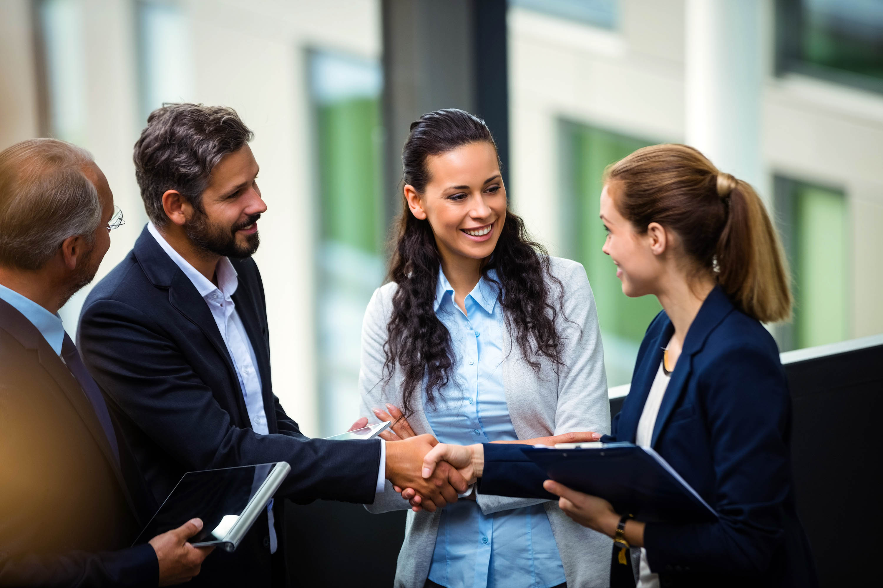 Businesswoman shaking hands with a businessman while two colleagues look on during a discussion in a modern office.