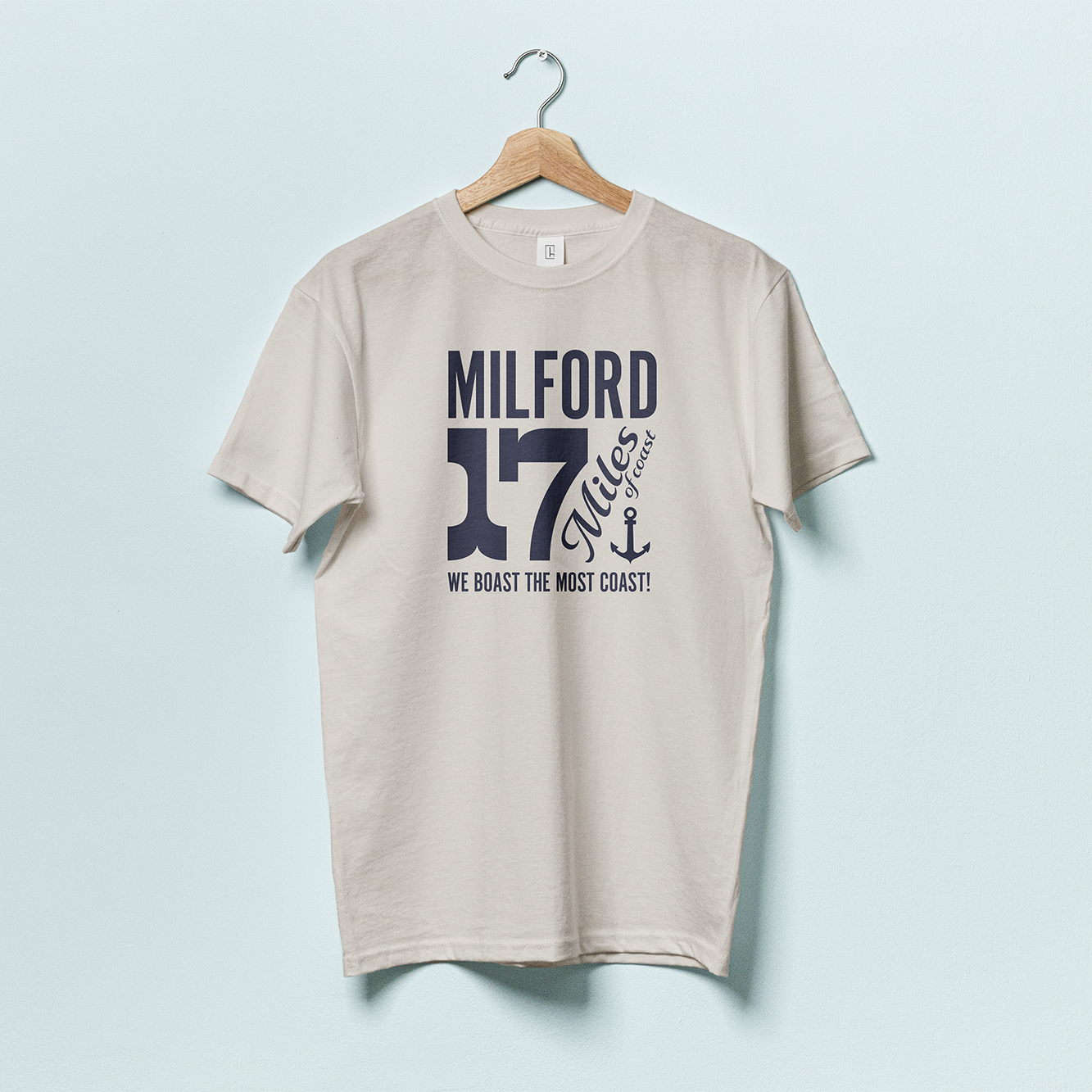 A gray t shirt with black text featuring the town name "Milford" and a large "17 Miles of Coast" with an anchor and the phrase "WE BOAST THE MOST COAST"