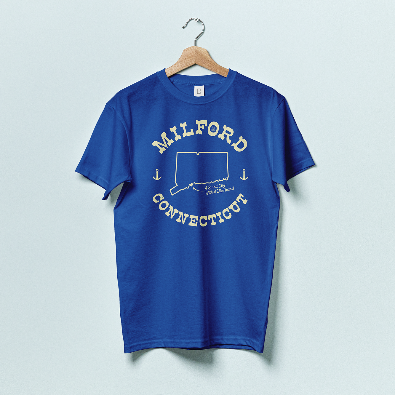 A blue t-shirt with yellow text forming a circle that reads "MILFORD CONNECTICUT" with an outline of the state of Connecticut in the middle and two anchors on the side