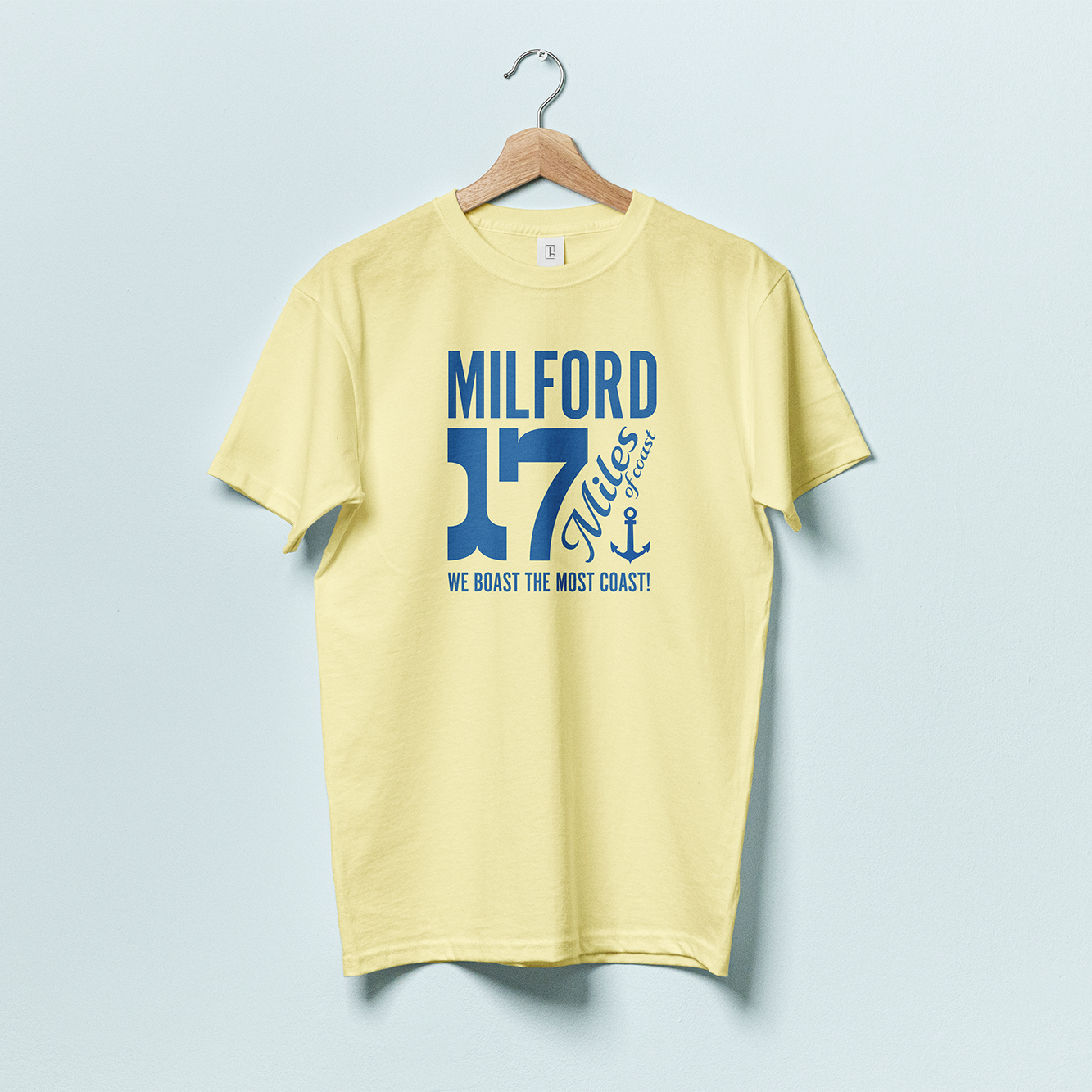 A yellow t shirt with blue text featuring the town name "Milford" and a large "17 Miles of Coast" with an anchor and the phrase "WE BOAST THE MOST COAST"