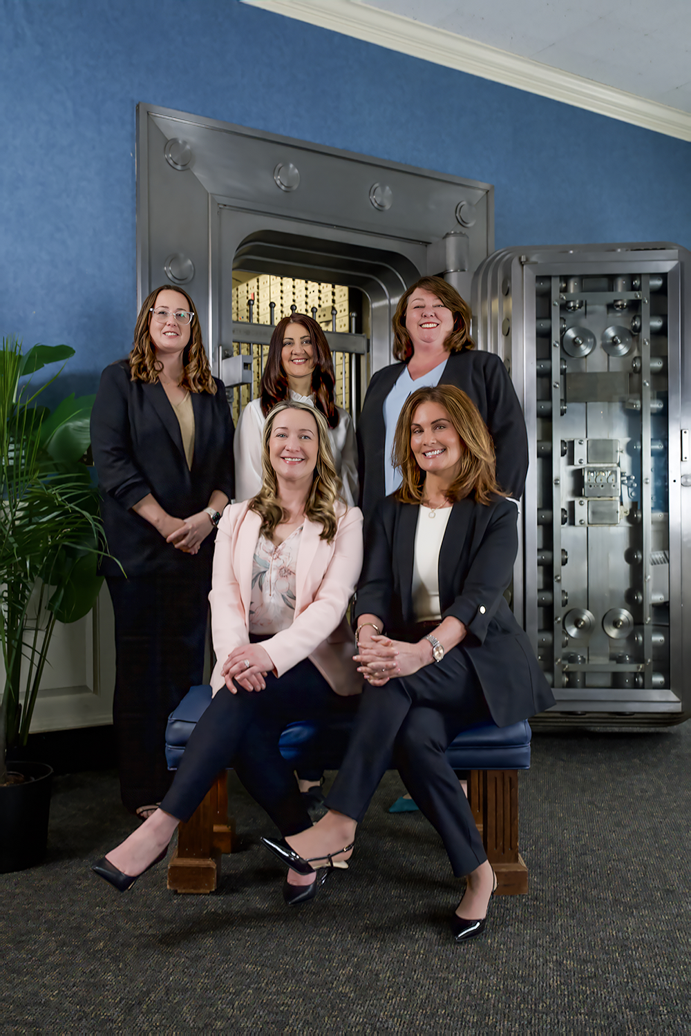 five professionally dressed women posing in front of a bank vault