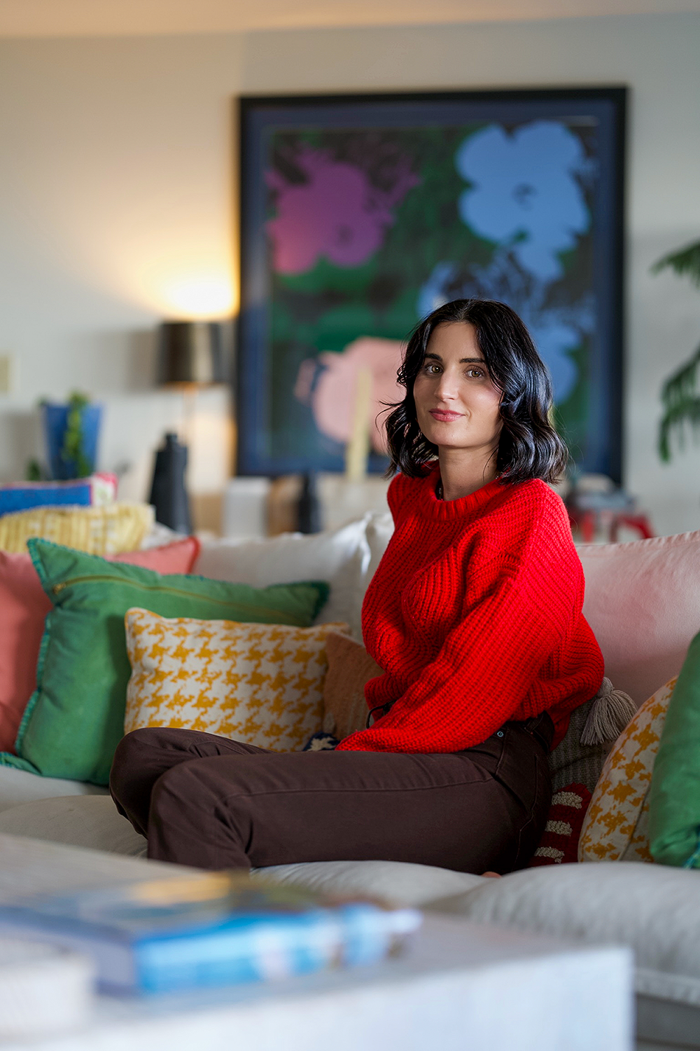 a woman in focus sitting on a couch wearing a bright red sweater