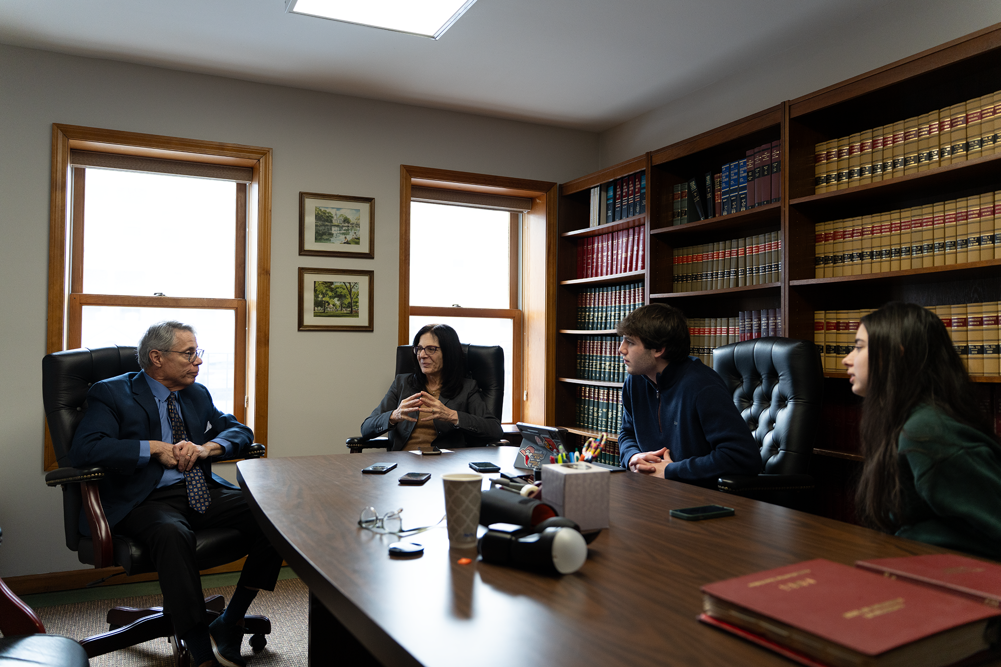 four people sitting around a conference table, with a decorated bookshelf in the background