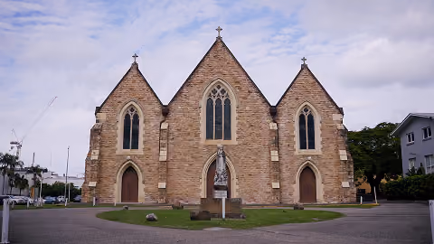 Front view of a stone church with three pointed roofs and arched windows and doors.