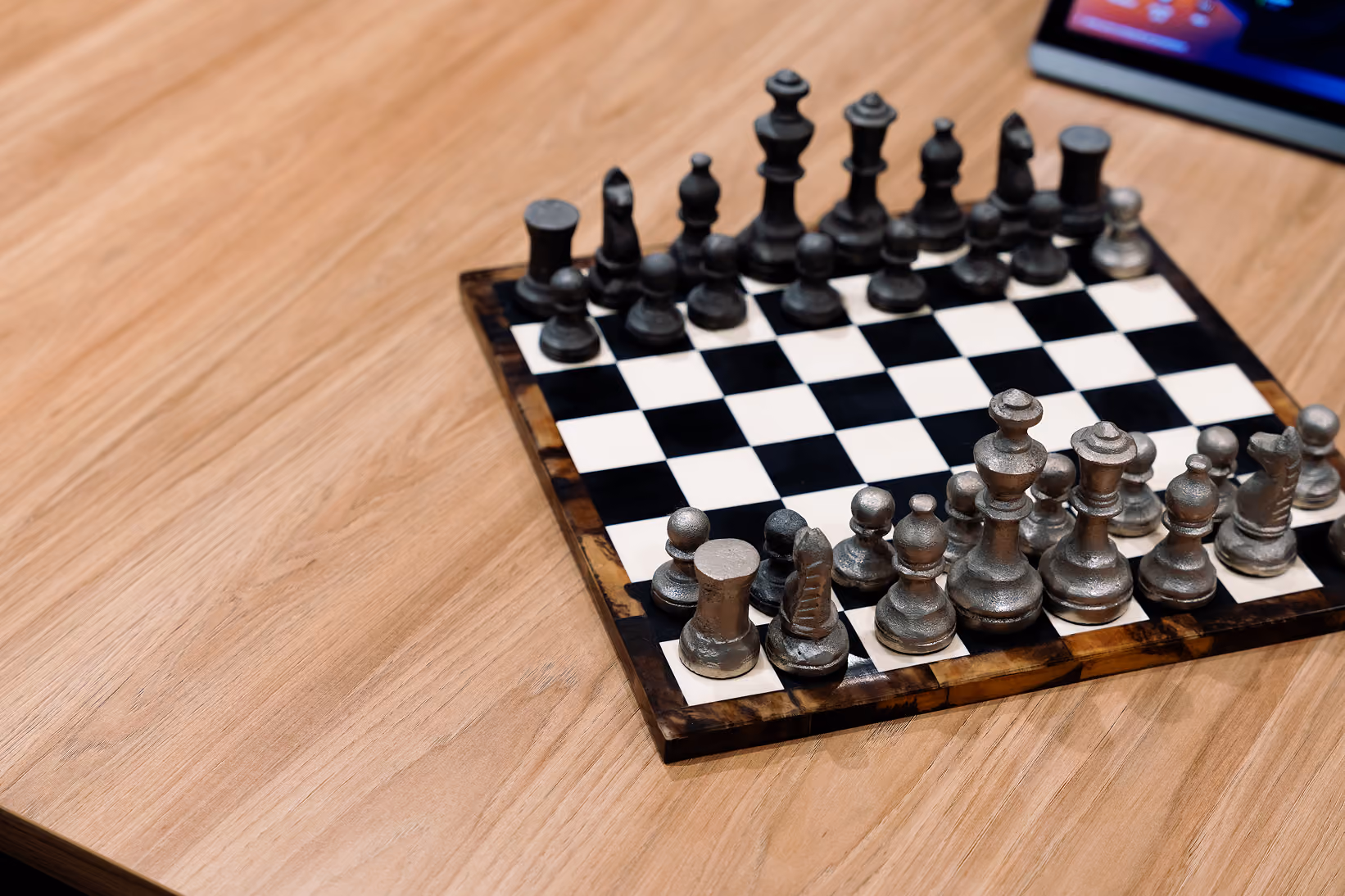 Metal chess pieces set up on a black and white checkered board on a wooden surface.