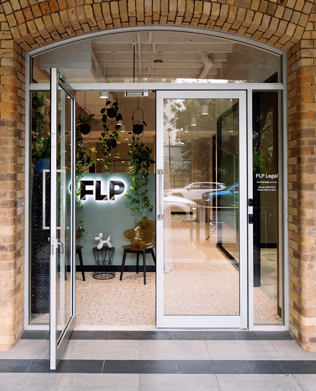 Glass entrance door to FLP Legal office with hanging plants, chairs, and logo inside.