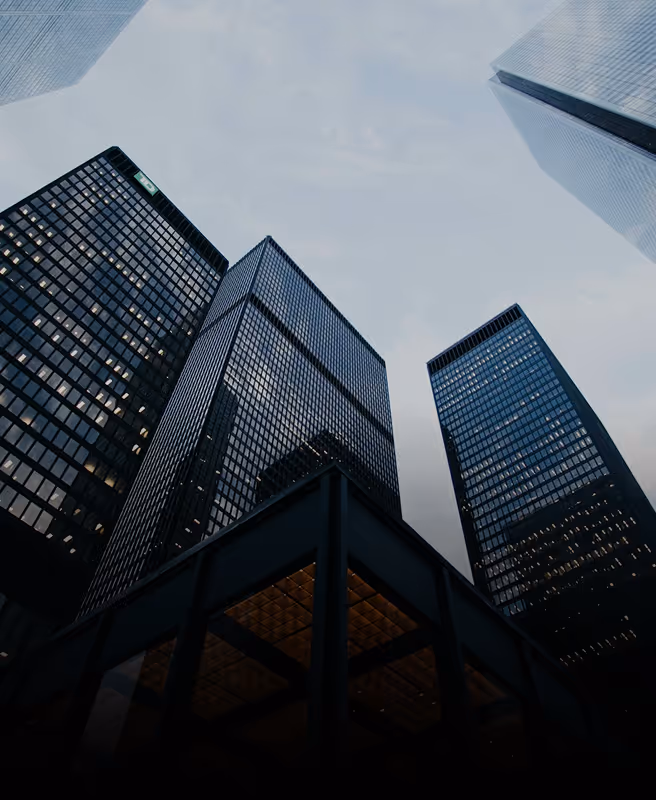 Low-angle view of tall modern office buildings with reflective glass windows against a cloudy sky.