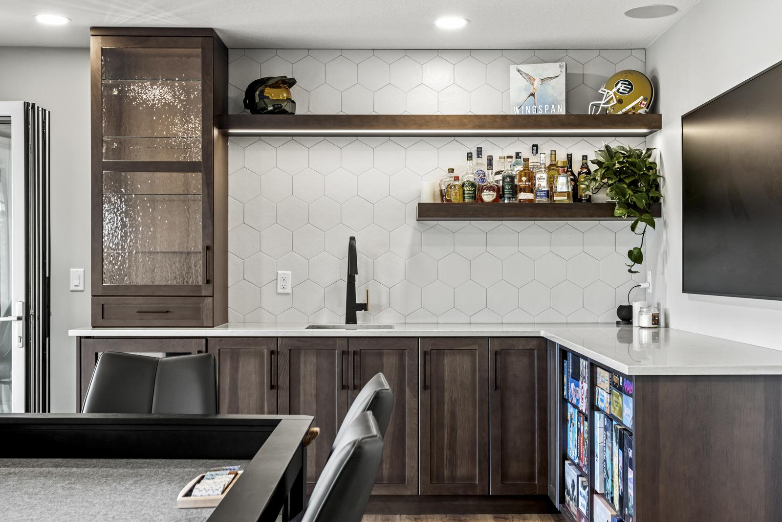Modern home bar with dark wood cabinets, hex tile backsplash, shelves with liquor and decor, and a sink.