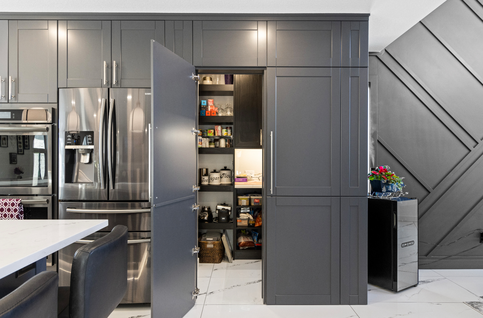 Modern kitchen with open pantry door showing shelves stocked with jars, cans, and containers.