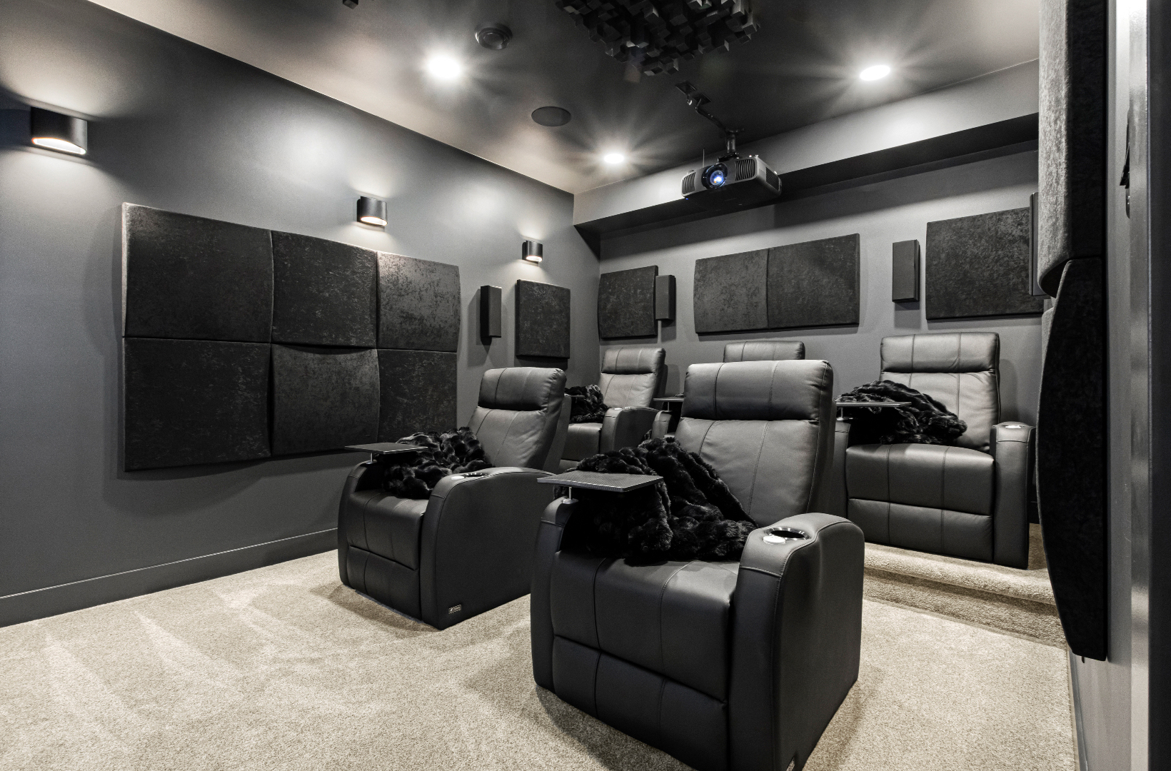 Modern home theater with four black leather recliners and sound panels on dark gray walls.