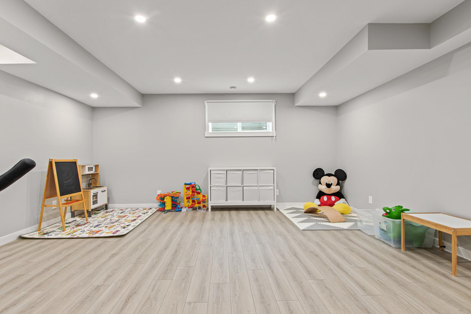 Bright children's playroom with toys, a chalkboard, storage unit, Mickey Mouse plush, and a small table.