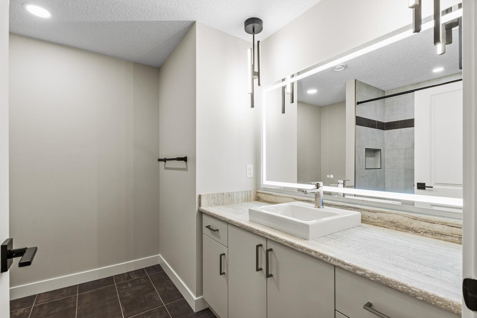 Modern bathroom with square sink, large mirror with light, and walk-in shower with tiled walls.