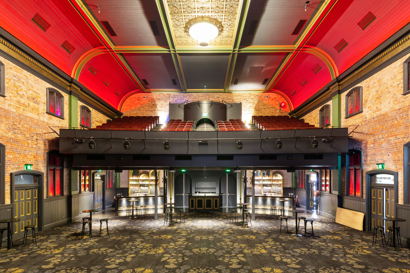Vintage-style theatre interior with red arched ceiling, balcony seating, bar area, and patterned carpeted floor.
