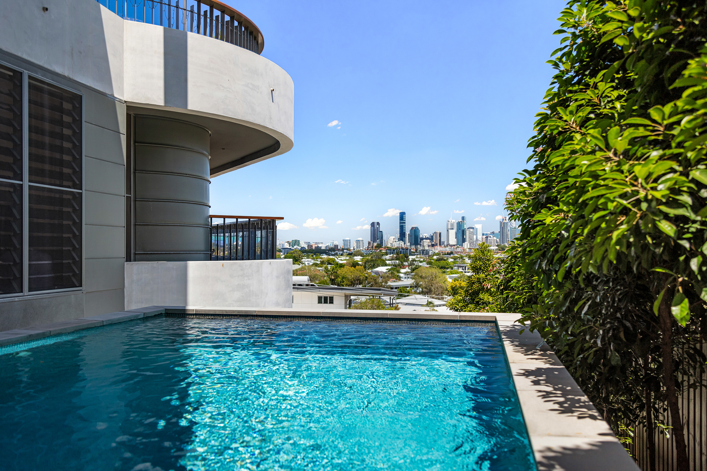 Outdoor pool beside a modern building with a clear view of a city skyline under a blue sky.