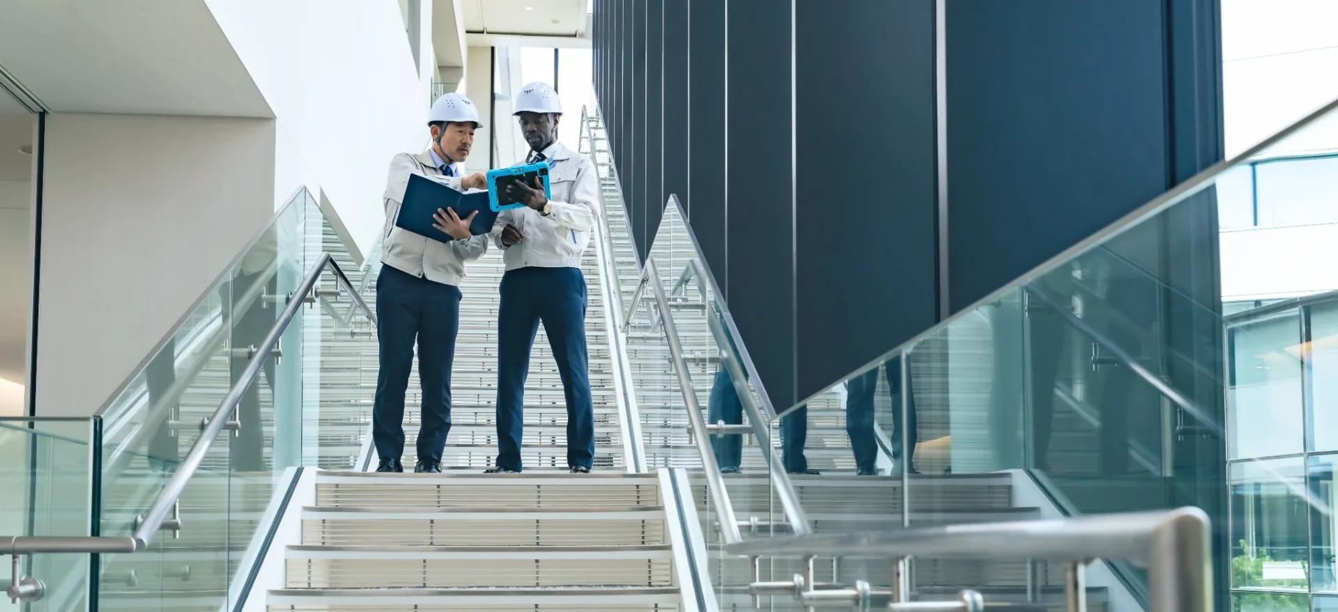 Two people in hard hats and clip boards walking down a stairs in newly built health centre 