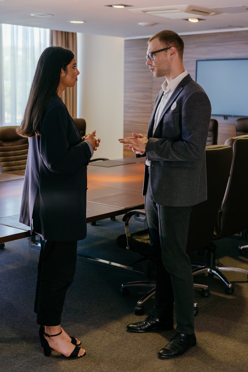 Two business professionals standing in an office conference room engaged in conversation.
