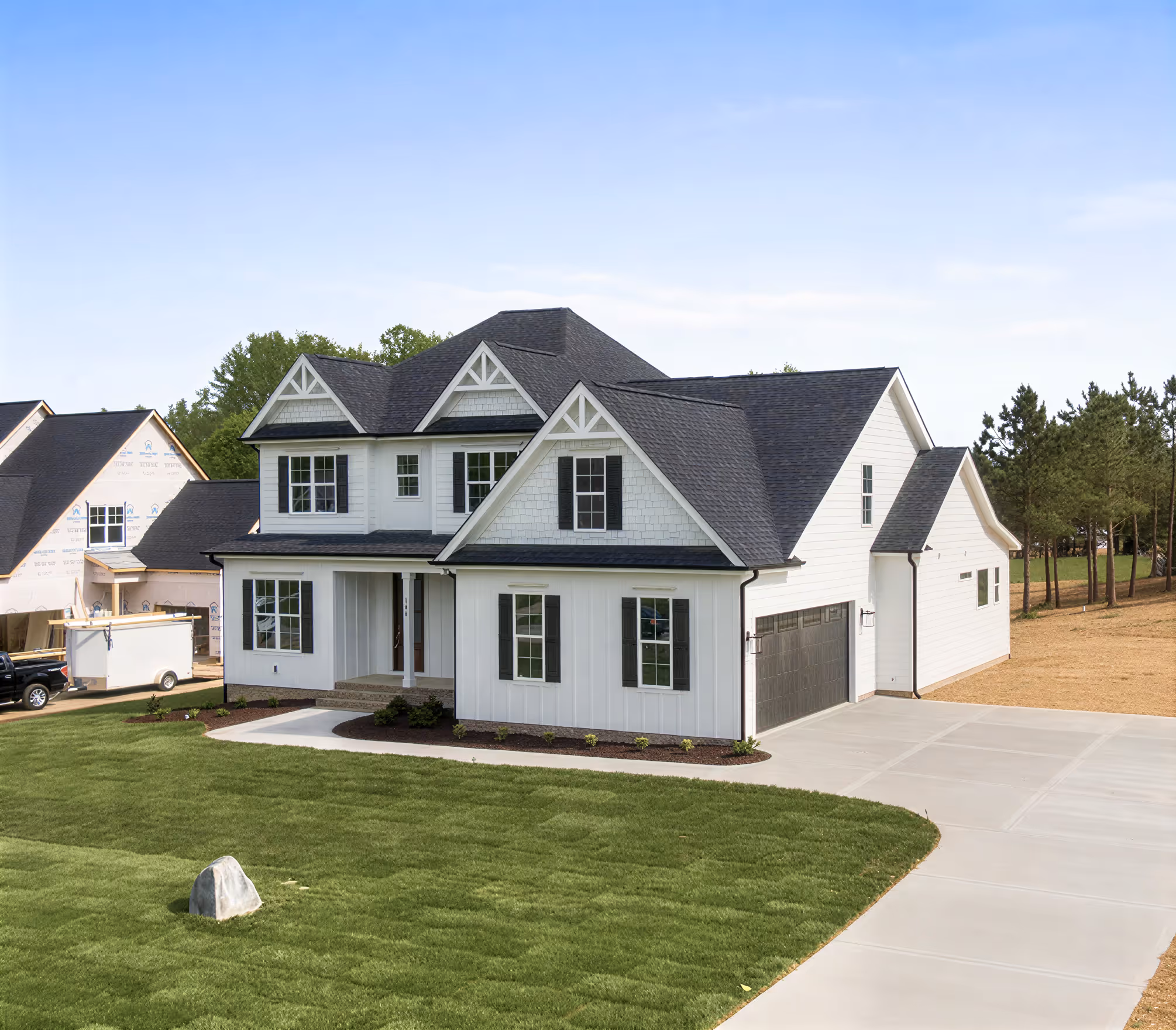 Modern two-story white house with dark roof, multiple gables, black shutters, a front porch, attached garage, and a freshly sodded lawn with a single rock.