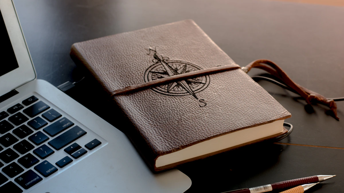 Leather notebook open beside a laptop in warm evening light, handwritten commission notes visible