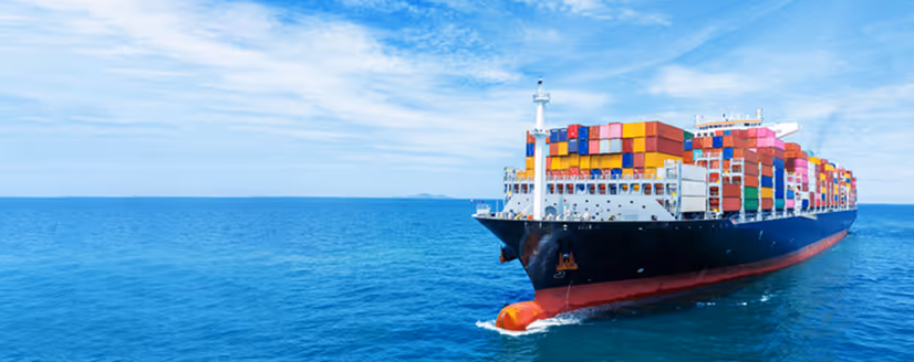 Large cargo ship loaded with multicolored shipping containers sailing on calm blue ocean under a partly cloudy sky.