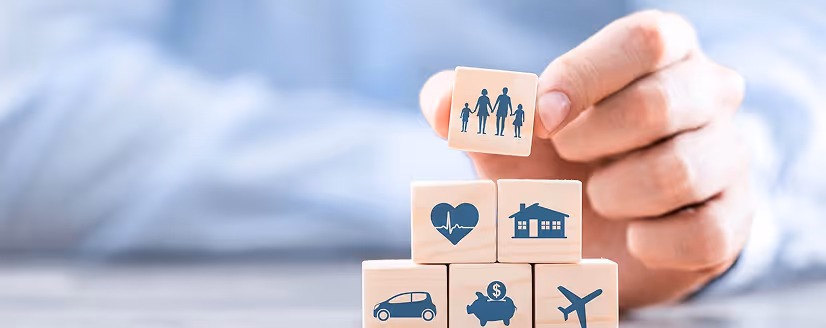 Hand stacking wooden blocks with icons representing family, health, home, car, savings, and travel.