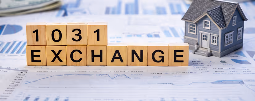 Wooden blocks spelling out '1031 EXCHANGE' placed on financial documents with a small model house nearby.