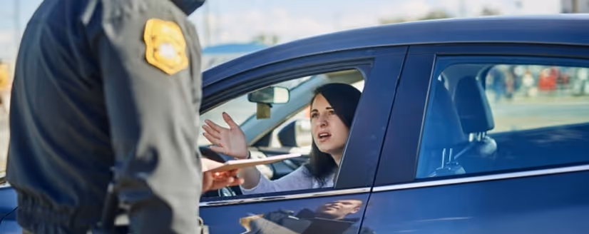 Woman in a car speaking with a police officer standing outside the vehicle.