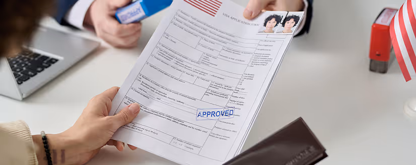 Hands holding a visa application form with passport photos and an approved stamp.