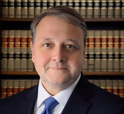 Christopher Callaghan in a suit and blue tie standing in front of shelves filled with law books.