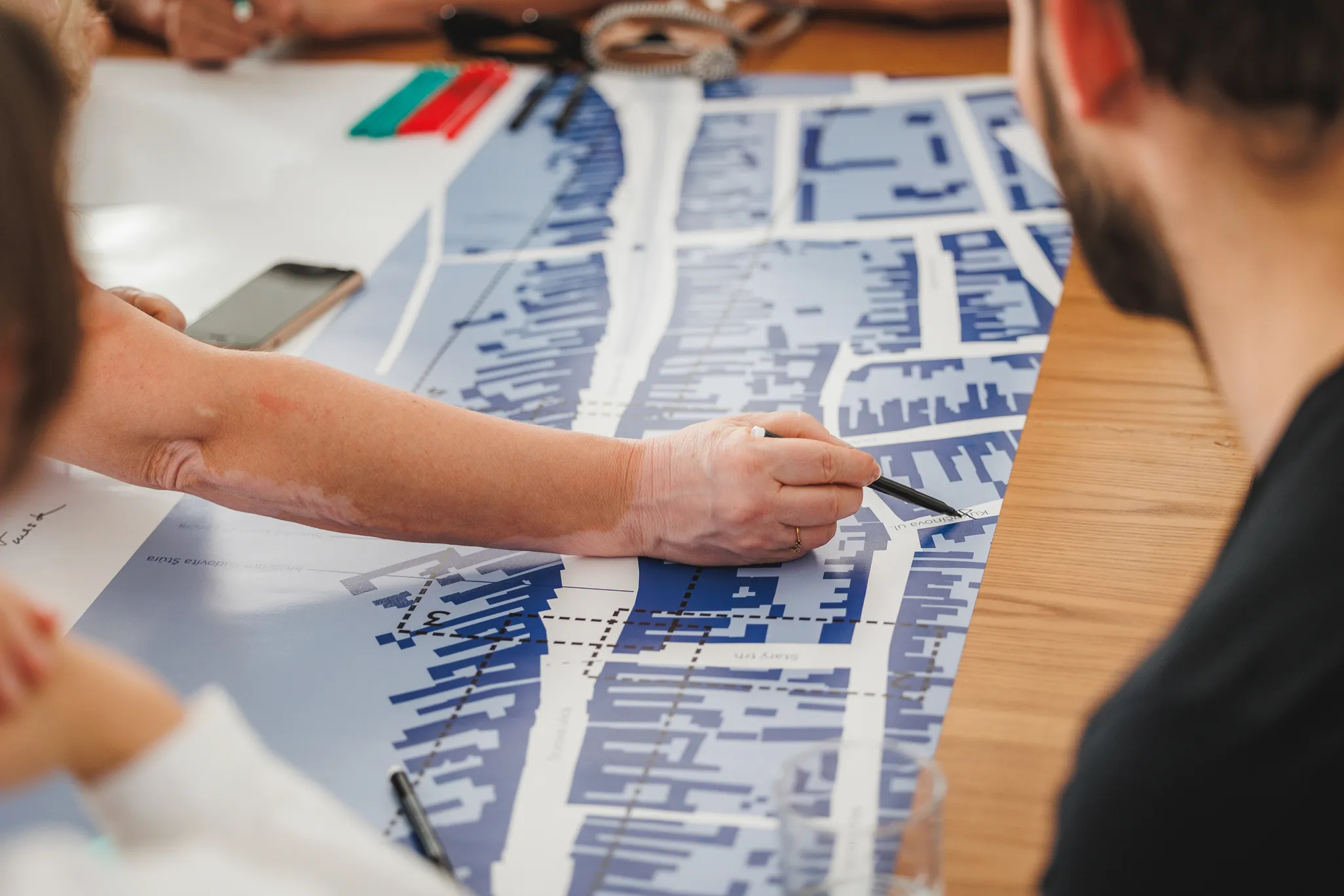 Ruky ľudí pracujúce na mape mesta rozloženú na stole počas diskusie.