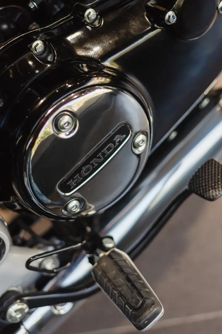 Close-up of a shiny black Honda motorcycle engine cover with mounting bolts and foot peg.