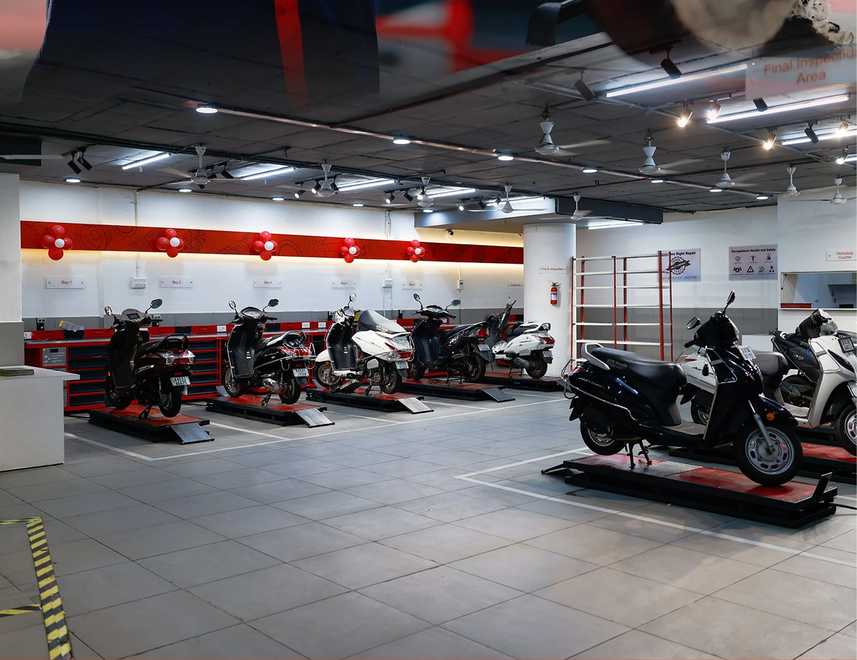 Indoor scooter service center with multiple scooters lined up on maintenance platforms under bright ceiling lights.
