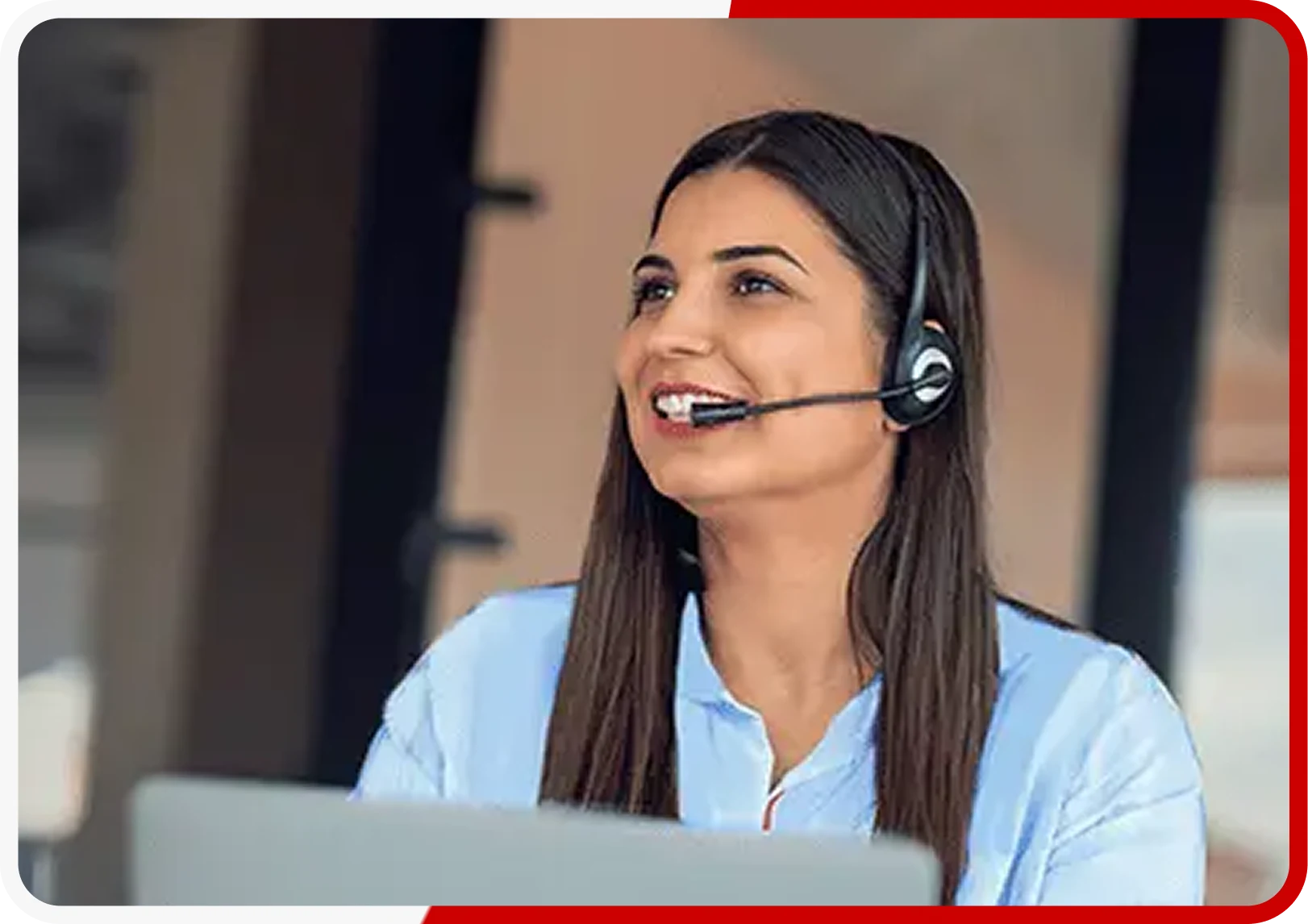 Smiling woman with headset working on a laptop in an office setting.